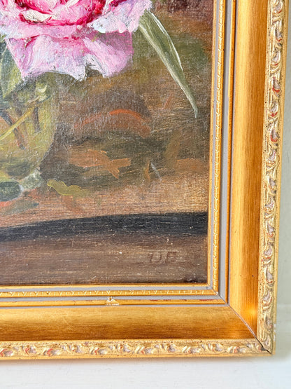 Close-up of a framed oil painting showing a pink flower with green leaves against a dark brown background, set in an ornate gold frame.