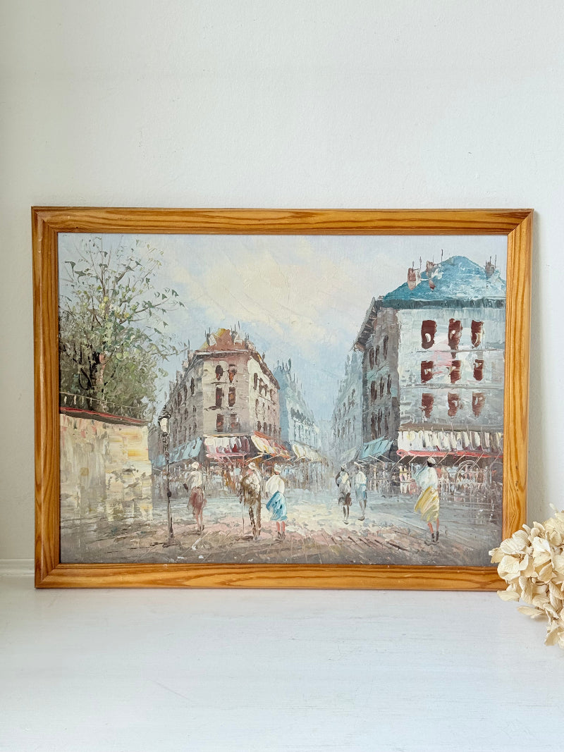 Vintage oil painting of European street scene with buildings and awnings in wooden frame photographed on a white surface


