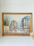 Vintage oil painting of European street scene with buildings and awnings in wooden frame photographed on a white surface

