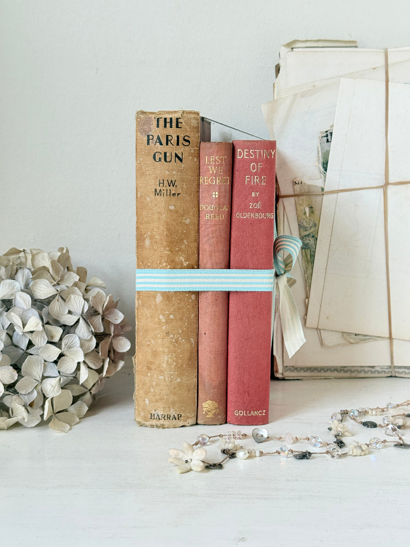 Three antique red books with aged spines tied with a turquoise striped ribbon on a white surface, styled with glass and beads