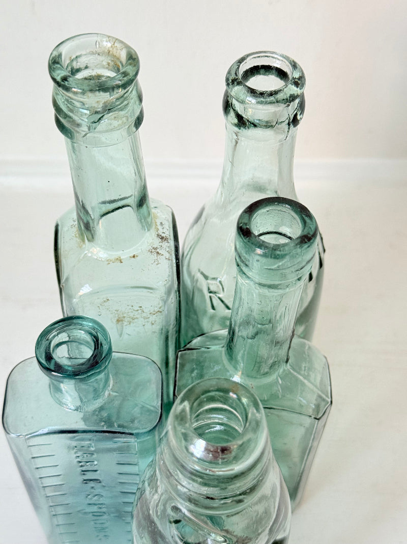 Set of five antique aqua green glass bottles with embossed lettering, photographed on a white surface
