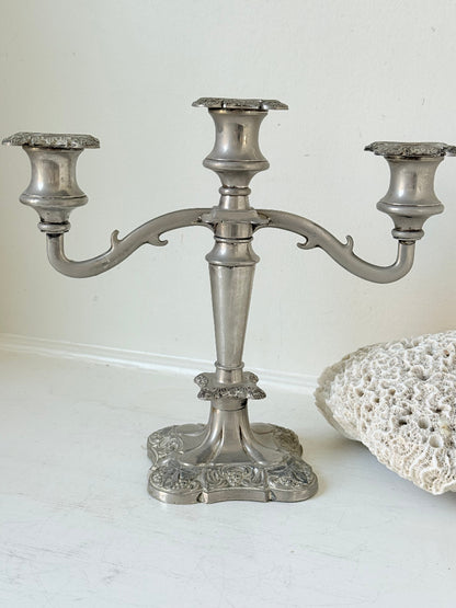 Vintage silver coloured three-arm candelabra with ornate base and soft patina, photographed on a white surface