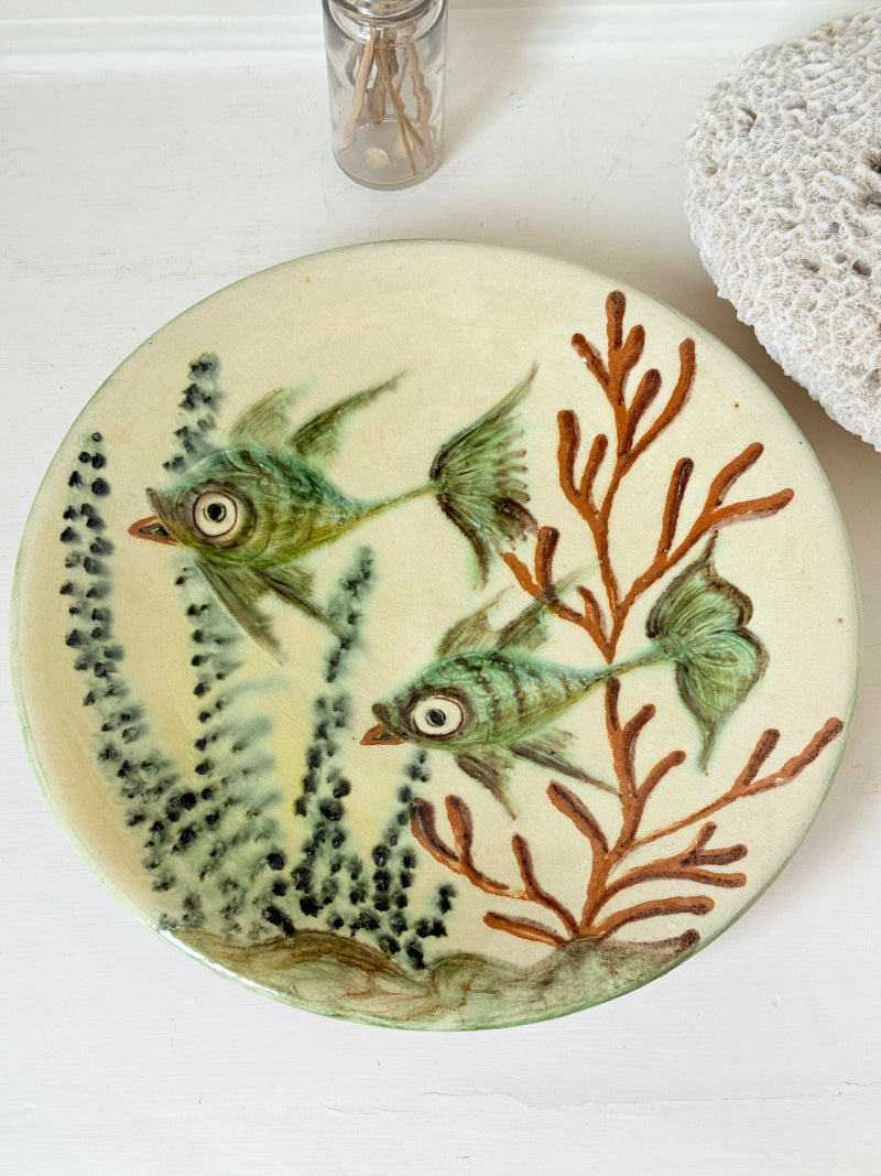 Puidgemont Spanish studio pottery plate with hand painted fish and coral design in green, turquoise, and terracotta tones, photographed on a white surface.