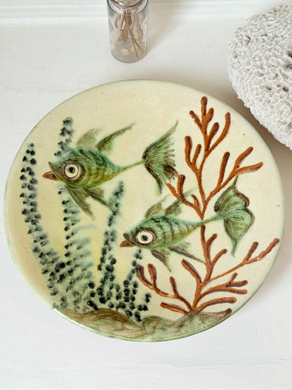 Puidgemont Spanish studio pottery plate with hand painted fish and coral design in green, turquoise, and terracotta tones, photographed on a white surface.