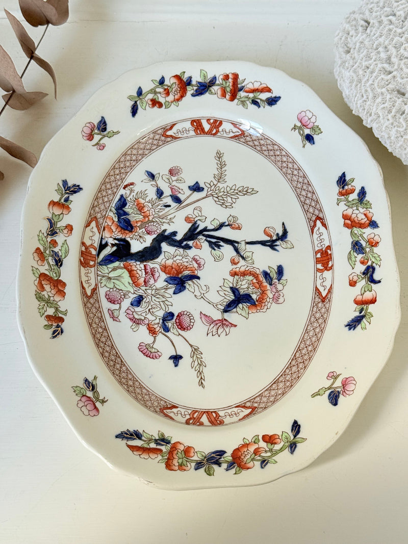 Vintage oval serving platter with chinoiserie style blue and red pattern photographed on a white surface