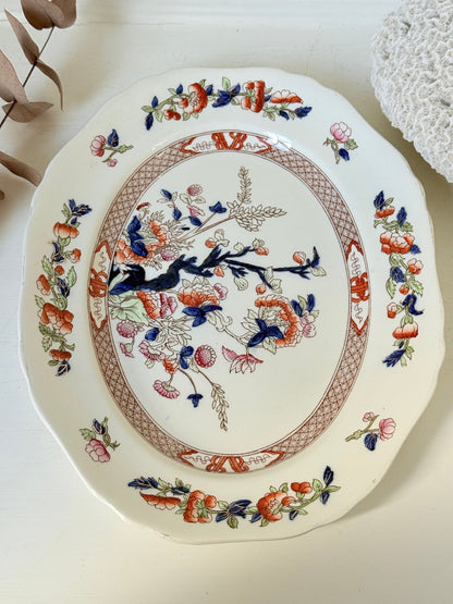 Vintage oval serving platter with chinoiserie style blue and red pattern photographed on a white surface