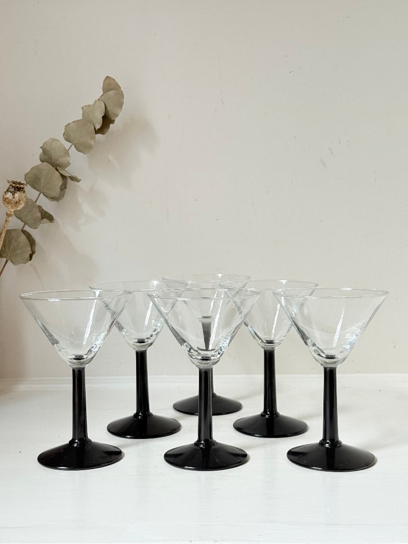 Set of six clear martini glasses with black stems, photographed on a white surface