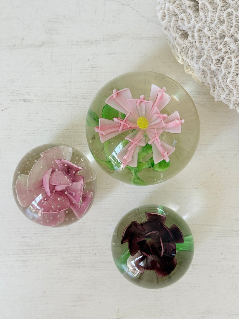 Trio of vintage glass paperweights with hand worked pink and plum floral detail, clear glass domes and green leaf decoration