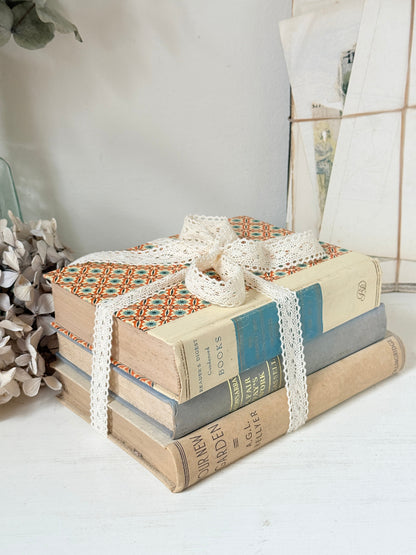 Bundle of vintage cream and blue cloth books with one patterned cover tied with ivory lace for shelf styling