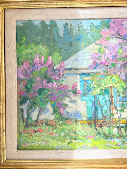 A framed impressionist oil painting depicting a cottage surrounded by vibrant pink and purple flowering trees and lush green foliage under a soft blue sky.