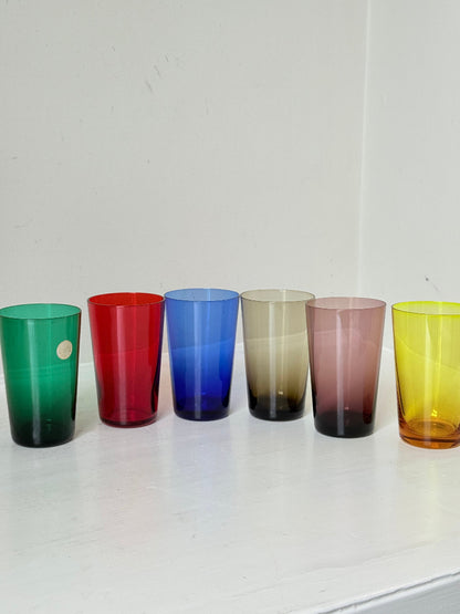 Set of six mid-20th century Boussu coloured glass beakers in rainbow hues, green with original label, photographed on white surface.