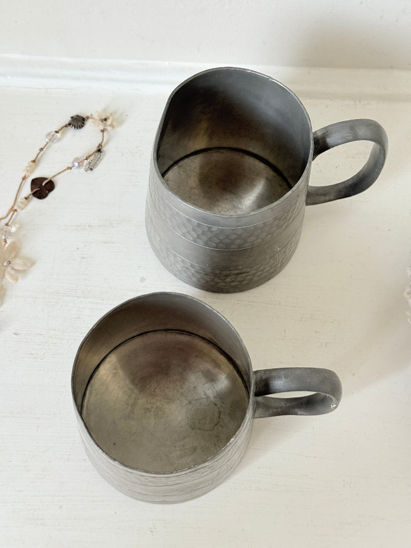 Pair of vintage pewter tankards with handles and textured detail, photographed on a white surface