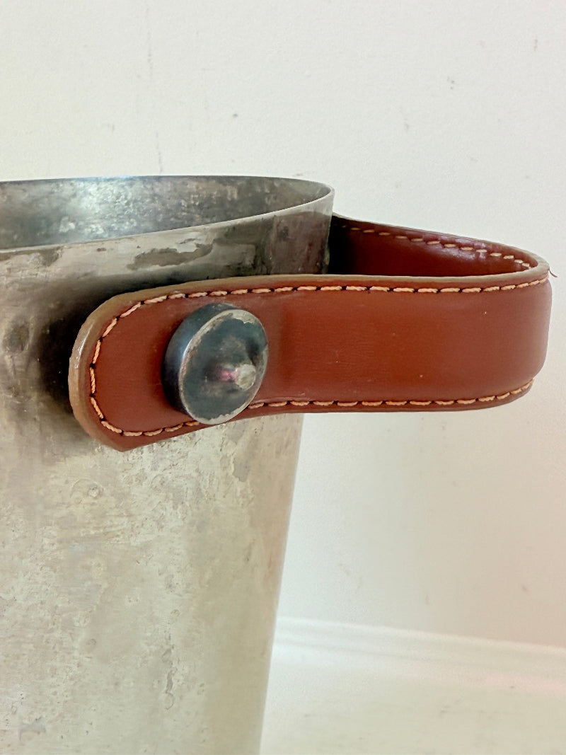 Vintage metal wine cooler with leather handles and tapered form, photographed on white surface.