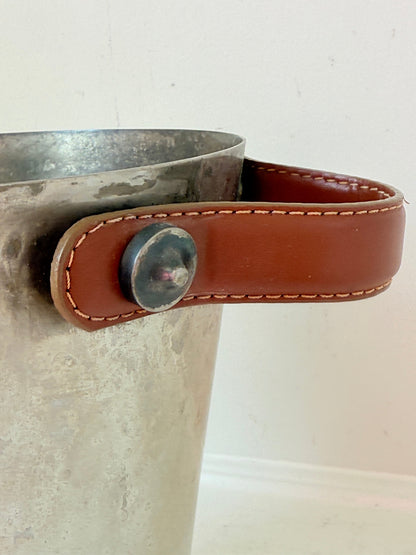 Vintage metal wine cooler with leather handles and tapered form, photographed on white surface.