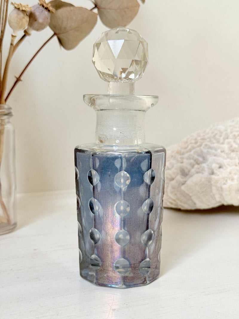 Vintage decagon iridescent glass perfume bottle with raised dot pattern and clear faceted stopper, photographed on a white surface