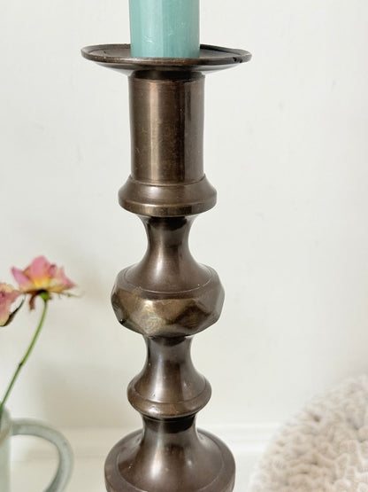 Bronze coloured vintage candlestick with bobbin stem and shaped base styled with taper candle on white surface