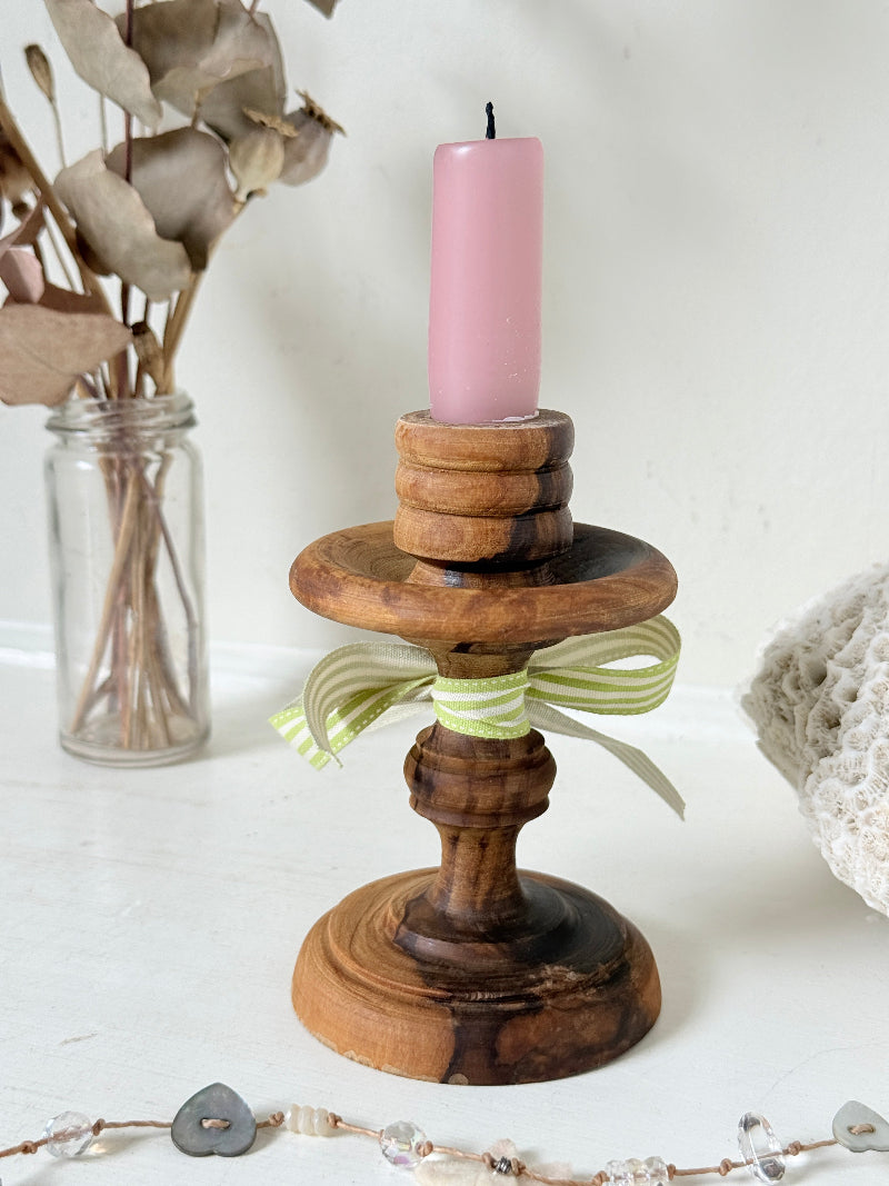 Vintage olivewood candlestick photographed on a white surface, turned wooden stem with warm grain and wide base holding a pink taper candle