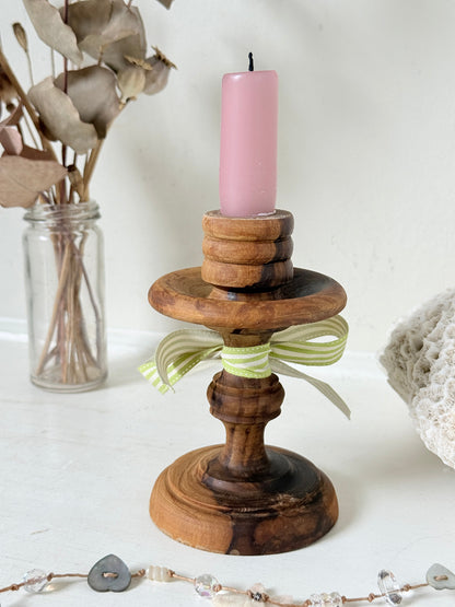 Vintage olivewood candlestick photographed on a white surface, turned wooden stem with warm grain and wide base holding a pink taper candle