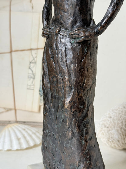 Solid bronze figure of a standing semi nude woman with upswept hair on a white marble base