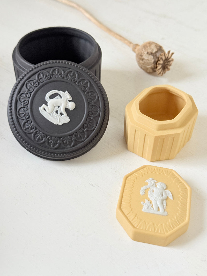 Pair of vintage Wedgwood Jasperware trinket pots in black and yellow with white relief decoration, photographed on a white surface