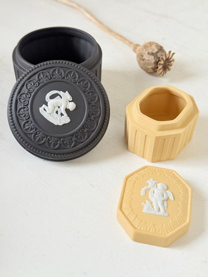 Pair of vintage Wedgwood Jasperware trinket pots in black and yellow with white relief decoration, photographed on a white surface