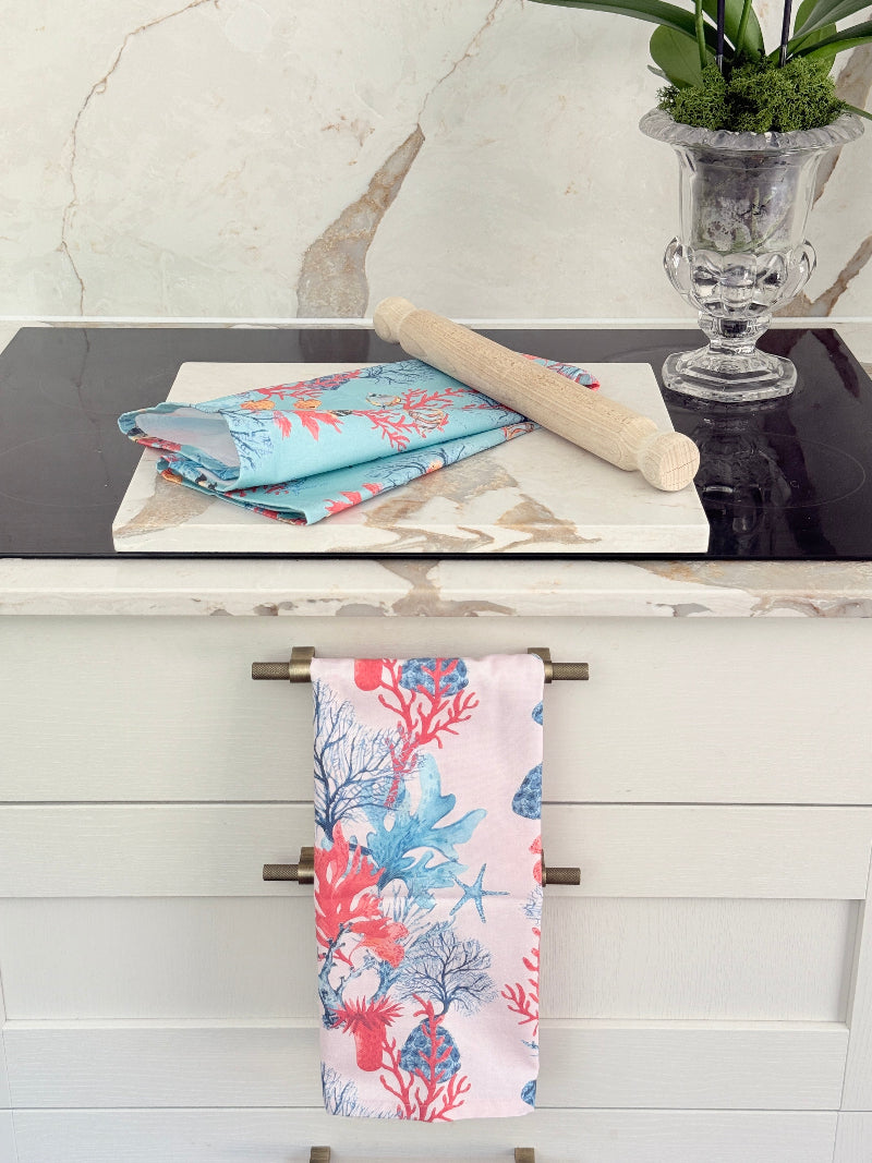 The Blue Loft coral reef cotton tea towels in turquoise and pale pink with coastal marine pattern photographed on a stone surface.