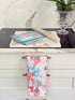 The Blue Loft coral reef cotton tea towels in turquoise and pale pink with coastal marine pattern photographed on a stone surface.