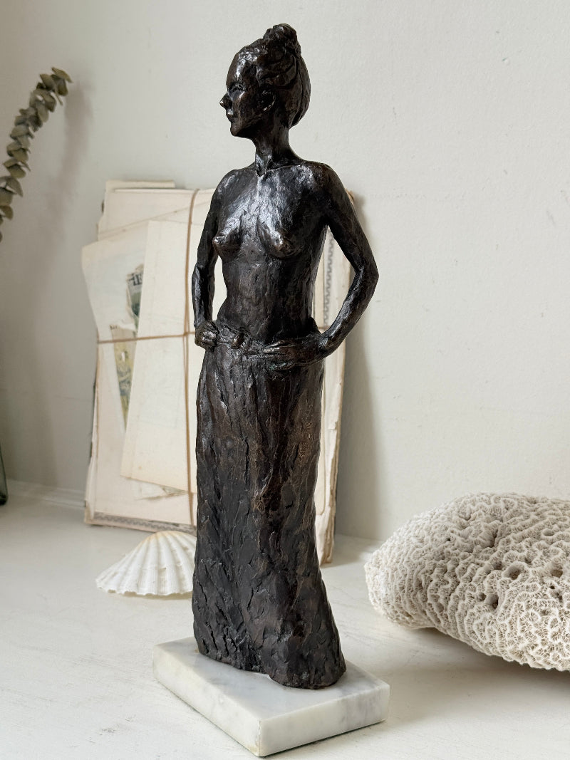 Solid bronze figure of a standing semi nude woman with upswept hair on a white marble base