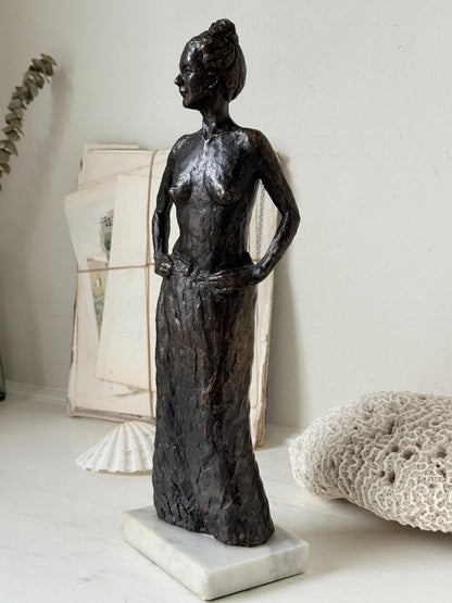 Solid bronze figure of a standing semi nude woman with upswept hair on a white marble base