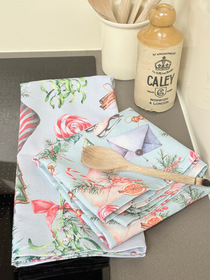 Pair of pastel blue festive tea towels with candy cane and ribbon print, folded, photographed on a kitchen worktop