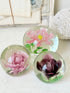 Trio of vintage glass paperweights with hand worked pink and plum floral detail, clear glass domes and green leaf decoration