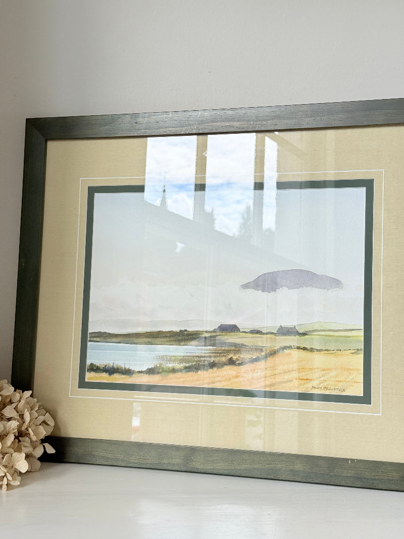 Framed Scottish watercolour coastal landscape by Martin W. M. Prentice in green frame with double mount, on white surface.