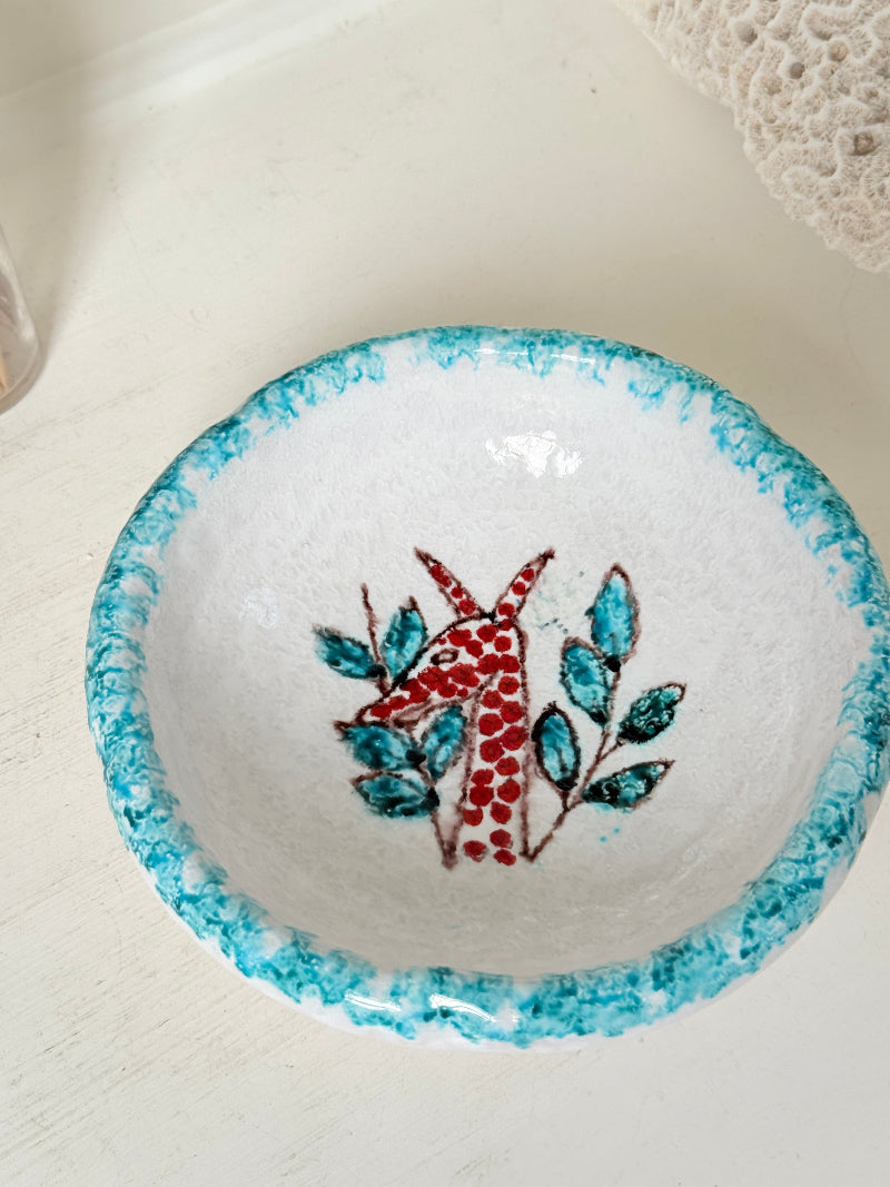 Vintage studio pottery bowl with turquoise rim and red hand painted giraffe motif, photographed on a white surface