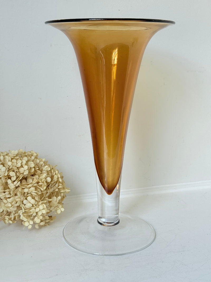 Tall mid-century amber trumpet vase with flared rim and clear glass foot, styled against a neutral background