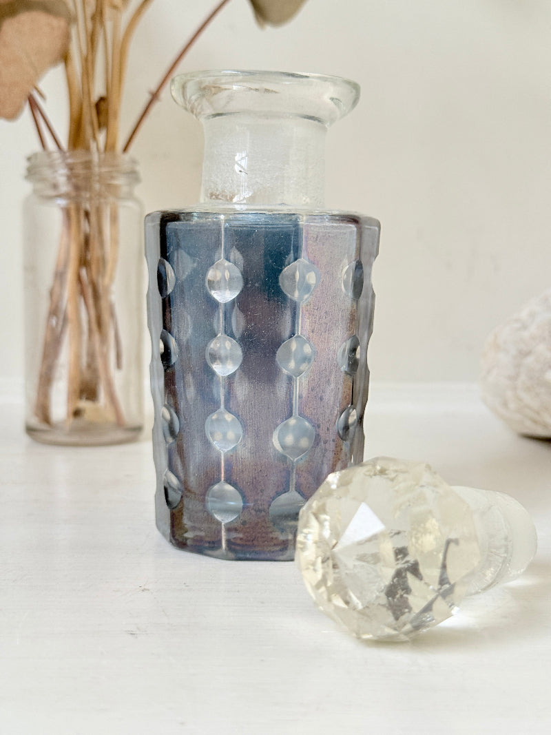 Vintage decagon iridescent glass perfume bottle with raised dot pattern and clear faceted stopper, photographed on a white surface