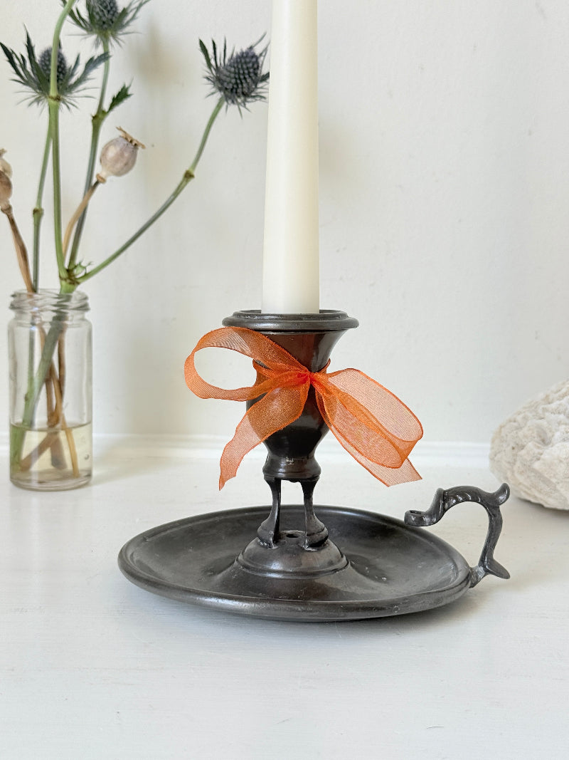 Vintage pewter chamberstick with handle and circular tray, photographed on a white surface
