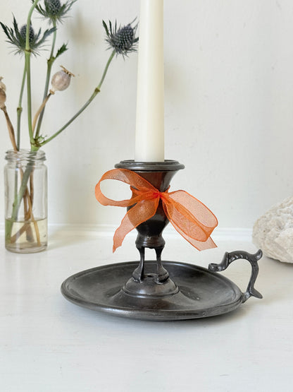 Vintage pewter chamberstick with handle and circular tray, photographed on a white surface