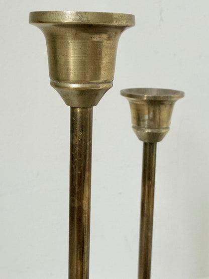 Set of 7 vintage brass candlesticks in graduated heights with aged brass finish styled with red ribbon on white surface