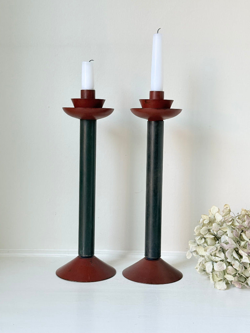 Pair of tall vintage metal candlesticks in black and burgundy, styled with white taper candles on a white surface.