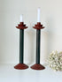 Pair of tall vintage metal candlesticks in black and burgundy, styled with white taper candles on a white surface.