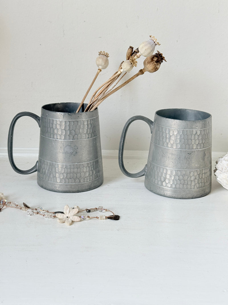 Pair of vintage pewter tankards with handles and textured detail, photographed on a white surface