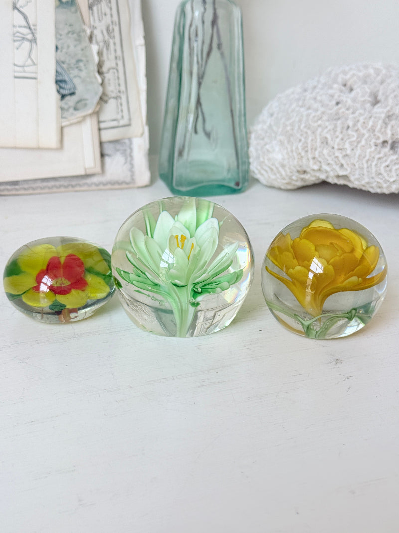 Trio of mixed flower glass paperweights in green, yellow and red, graduated in size, photographed on a white surface