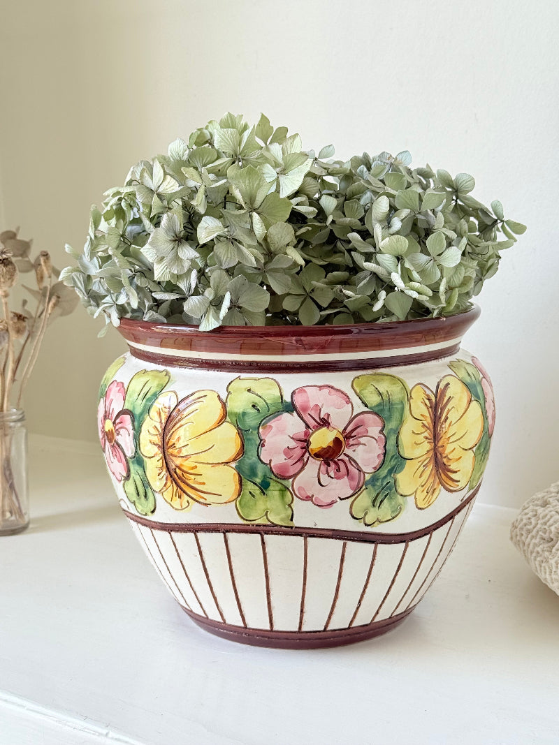Large European hand painted floral ceramic jardinière with yellow, pink and green flowers on a white base, styled on a white surface with dried foliage.