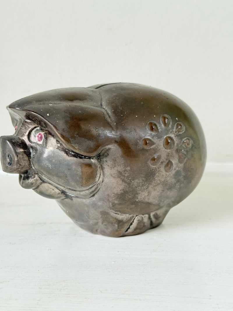 Vintage cast metal piggy bank in the shape of a pig with red painted eyes, photographed on a white surface