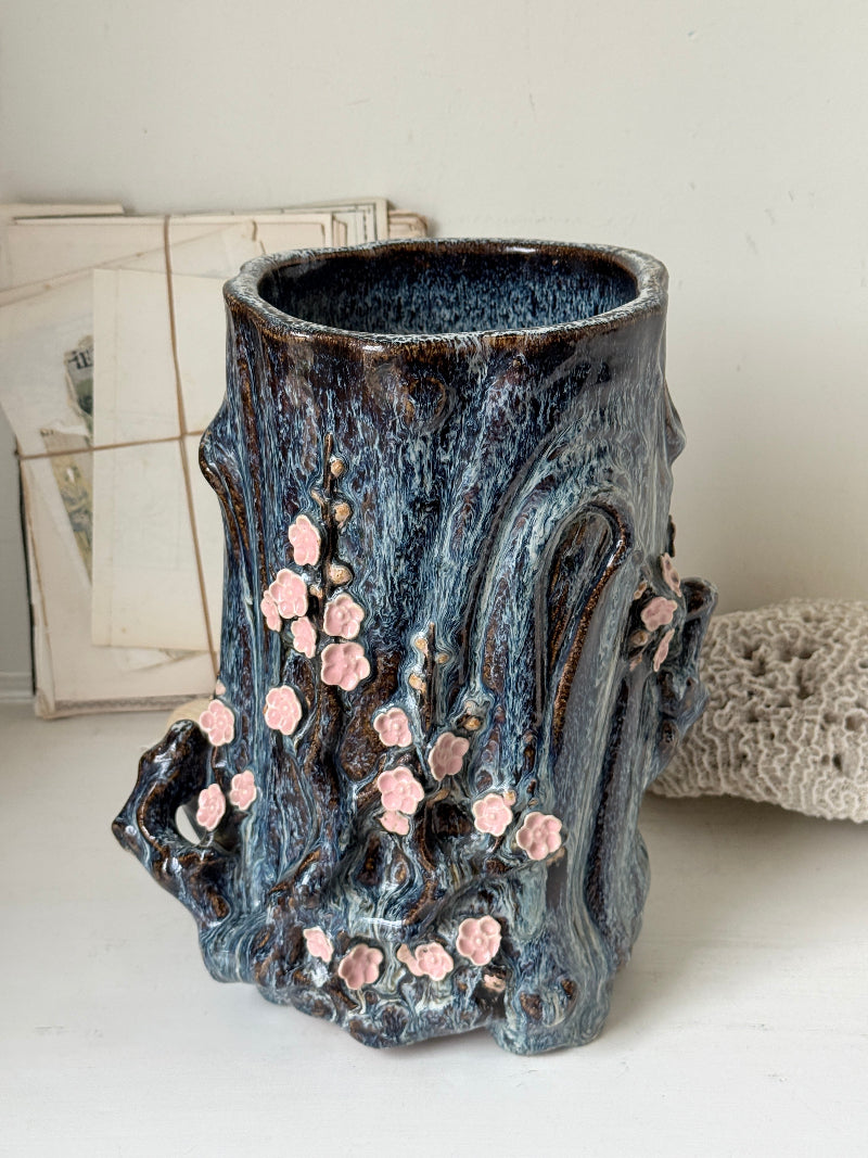 Large ceramic tree trunk vase with applied pink cherry blossom detail, textured bark form and dark drip glaze