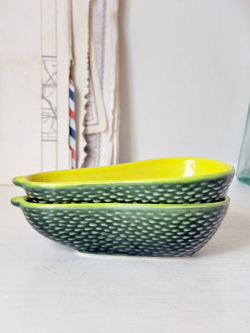 Two stacked ceramic bowls with a textured green exterior and a bright yellow interior, set on a white surface with a softly blurred background.