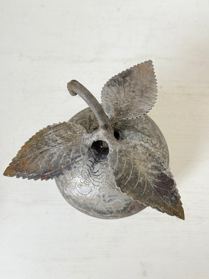 An antique-style metal apple lantern with engraved details, featuring three leaf-shaped handles and a curved neck, shown on a light off-white background.
