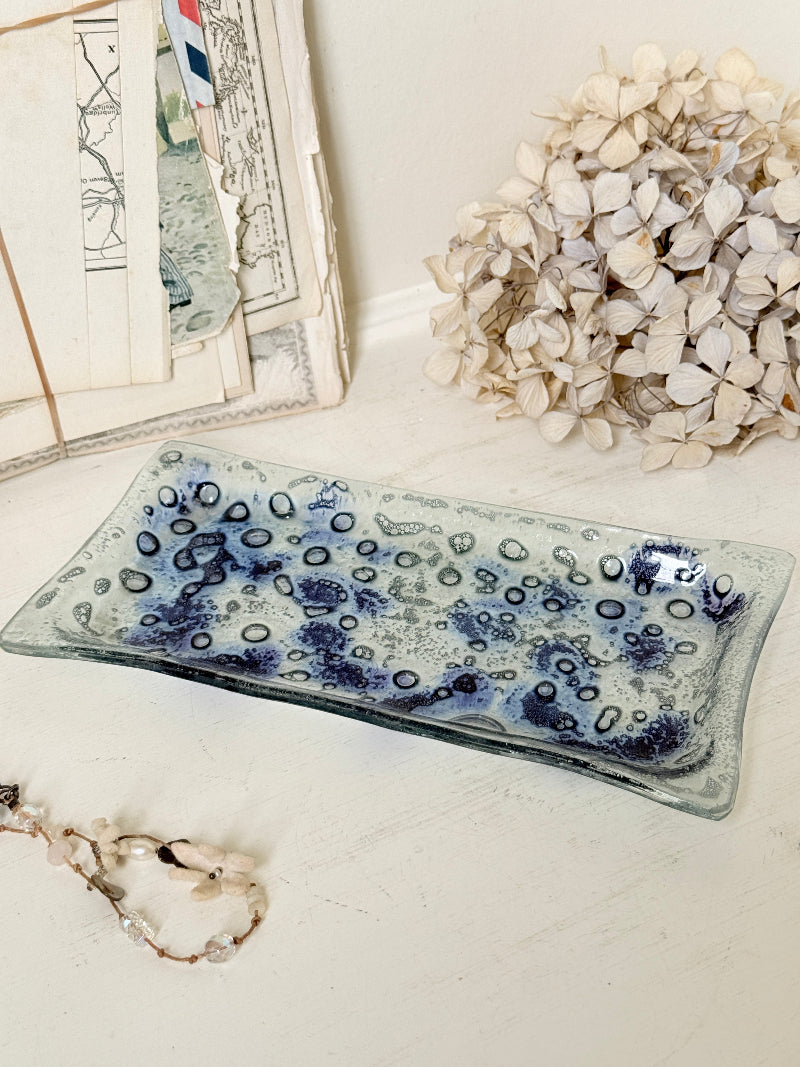 A rectangular glass tray with a blue and white spotted pattern, styled on a white surface with dried flowers and vintage papers in the background.