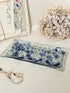 A rectangular glass tray with a blue and white spotted pattern, styled on a white surface with dried flowers and vintage papers in the background.