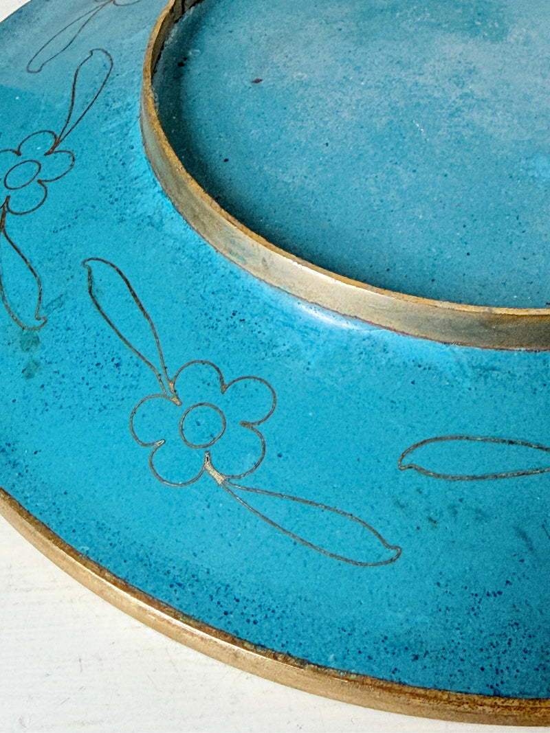 A close-up of a turquoise blue ceramic plate with hand-painted brown floral outlines and a metallic gold-toned rim.